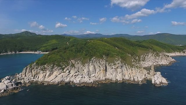 Aerial shot moving along the coastline of deep blue sea along a dramatic cliff edge on sunny day