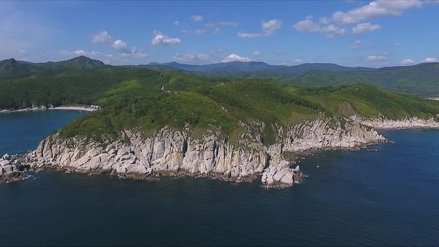 Aerial shot moving along the coastline of deep blue sea along a dramatic cliff edge on sunny day