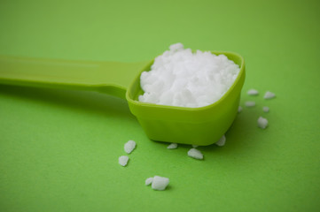 closeup of white salt grain in a green plastic spoon on green background