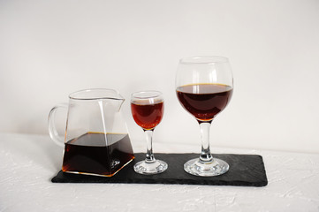 Coffee in a transparent serving teapot of two wine glasses for tasting. Served on a slate board on a white background.