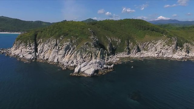 Aerial shot moving along the coastline of deep blue sea along a dramatic cliff edge on sunny day