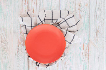 Empty coral circle plate on wooden table with linen napkin.