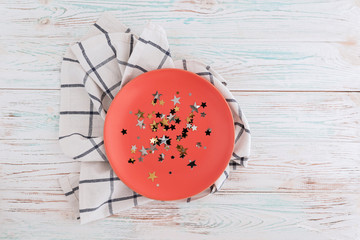 Coral circle plate with star confetti on wooden table with linen napkin.