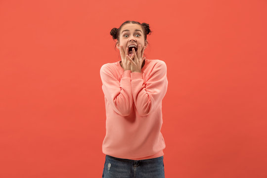 Delight. Beautiful female half-length front portrait isolated on coral studio backgroud. Young, emotional, smiling, surprised woman standing. Human emotions, facial expression concept. Trendy colors