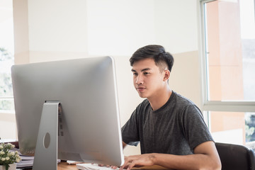Attractive Asian businessman / student young man sitting working busy for seaching information data internet at office technology center room near document report on desk