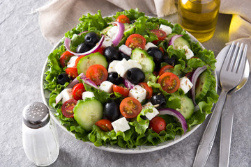 Fresh Greek salad in Plate with black olive,tomato,feta cheese, cucumber and onion on gray background. Top view. Copyspace