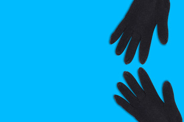 Pair of black warm woolen gloves on blue background with copy space for your text. Top view