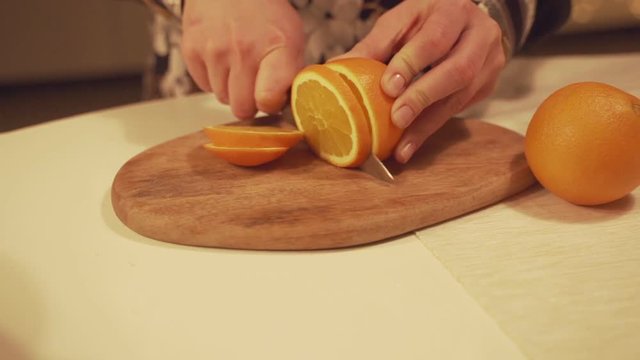 Feamale hands cutting orange on cutting board for homemade mulled wine with orange slices, cranberries, cinnamon.