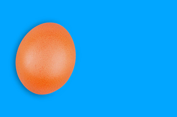 Single raw brown egg on blue background with copy space for your text