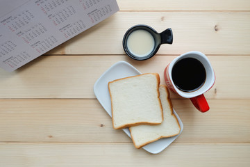 Top view and close up: Slices of bread with sweet milk, red mug of hot coffee, calendar on wooden background. Breakfast concept. 
