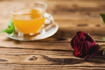 Glass cup with green tea and mint near red rose on sprig on old wooden table. Saint Valentine's Day concept