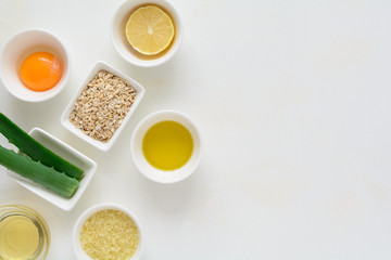 Fresh ingredients for homemade effective acne remedies on white background. Honey, sea salt, egg yolk, olive oil, oat, lemon and aloe. Flat lay. Copy space