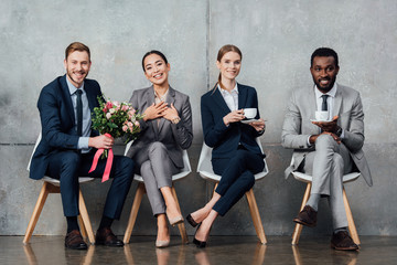 smiling multiethnic businesspeople sitting with flowers and coffee in office