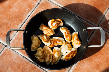 Flat lay image above traditional polish meal pirogi in the frying pan on the table. Delicious dough meal prepared on old way