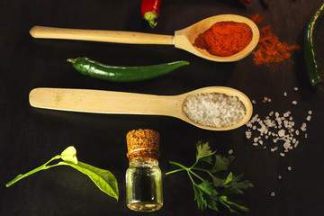 Hot chili peppers and spices in wooden spoons on a dark background.