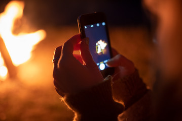 Camping girl photographing a bonfire on the phone ( phone in hand)