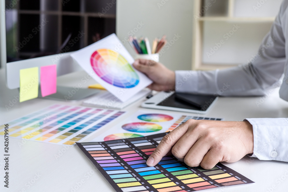 Poster Image of male creative graphic designer working on color selection and drawing on graphics tablet at workplace with work tools and accessories