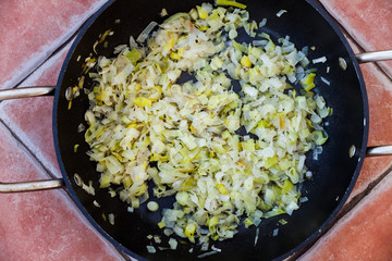 Top view of metal frying pan filled with sliced onions and paprika in oil. Preparing vegetables in the dishware. Cooking vegetarian food