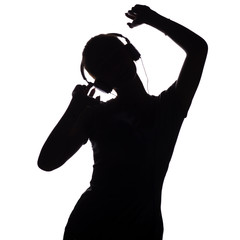 silhouette of a happy girl listening to music in headphones, figure of young woman with hands up relaxing on a white isolated background and dancing to the music