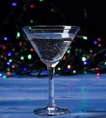 Cocktail glass on defocused garland colorful lights. Alcohol cocktail for winter party. Cocktail ideas concept. Easy recipes for winter alcoholic cocktail drinks. What to drink on christmas party