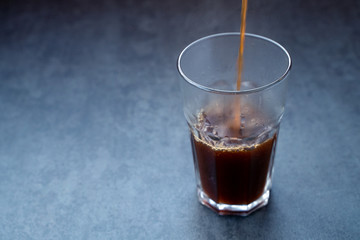 Pouring coffee into the glass on a dark gray stone table, copy space.
