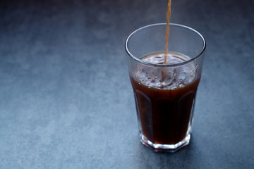 Pouring coffee into the glass on a dark gray stone table, copy space.