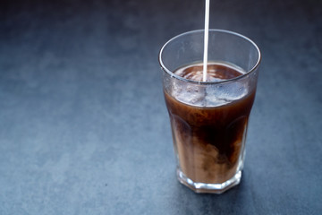 Pouring milk into coffee latte in the glass on a dark gray stone table, copy space.