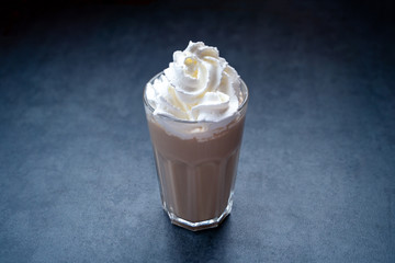 Cold hot coffee drink latte, with whipped cream in glass on a dark gray stone table, copy space.