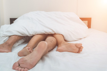 Close up of male and female feet on a white bed. The concept of loving couple having sex under white sheets in the bedroom. Sensual and intimate moment of lovers. Focus on male foot.