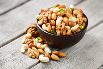 Wooden bowl with mixed nuts on a wooden gray background. Walnut, pistachios, almonds, hazelnuts and cashews, walnut.