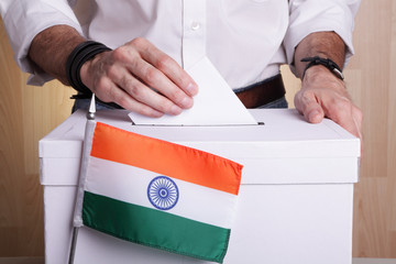 An Indian citizen inserting a ballot into a ballot box. India flag in front of it