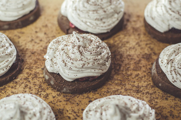 Chocolate cakes with egg white cream on the wooden board. Sweet and tasty homemade food.