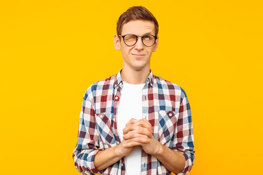 A focused man with glasses, a man in a plaid shirt, who folded his hands in prayer, asks for his need on a yellow background
