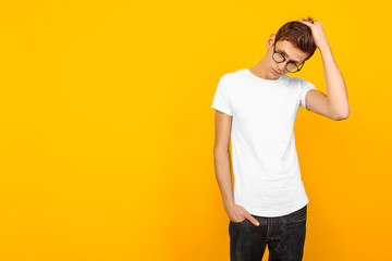 Handsome man in glasses, dressed in a white T-shirt, posing on a yellow background