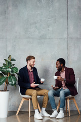 smiling men sitting and drinking coffee while talking in waiting hall