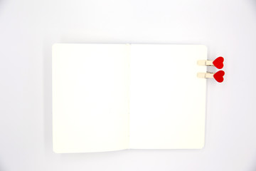 Two small heart pins on blank notebook on white isolated background