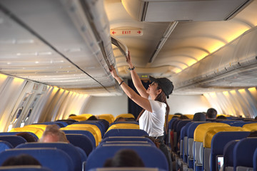 woman passenger traveler on boarding aircraft looking for empty overhead locker for luggage keep in...