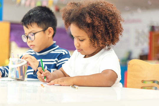Little toddler girl and boy concentrate  drawing together.  Asian boy and Mix African girl learn and play together in the pre-school class. Children enjoy hand writing. Friendship in class.