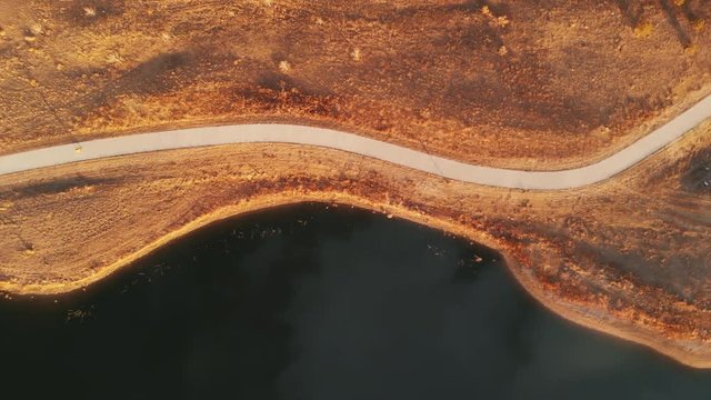 Electric Skateboarding on Curvy Path with Lake at Golden Hour Aerial Flyover View