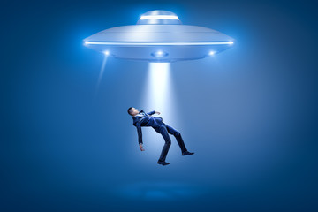 A businessman pulled toward an open hatch of a UFO by some invisible force.