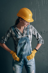 a strong-willed woman in a construction helmet, mittens, goggles and overalls is engaged in repair and construction work at home. concept of a strong and independent woman