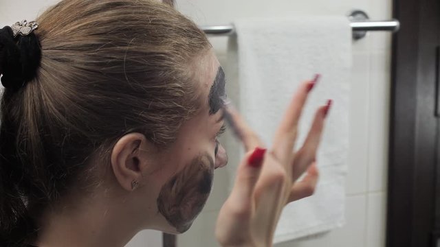 Teen girl applying facial black clay mud mask in bathroom. Skin care. Problem. Close up
