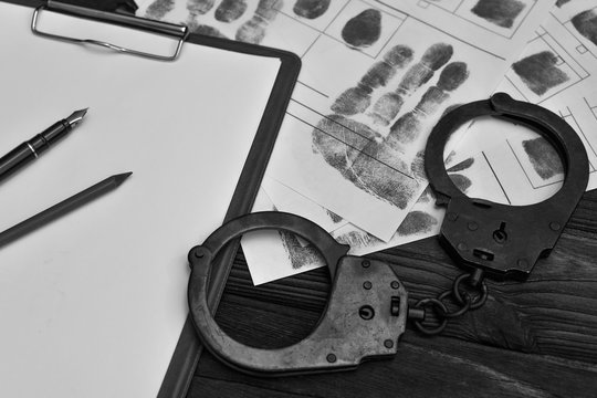 fingerprints, handcuffs, a piece of paper on a wooden background. crime, arrest, detention of criminals.