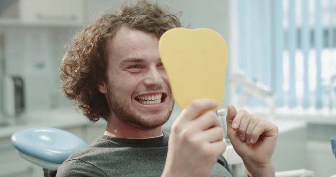 After the dentist visit smiling young patient in front of the mirror in dental clinic room after a oral hygiene procedure , he checked his smile. shoot on red epic