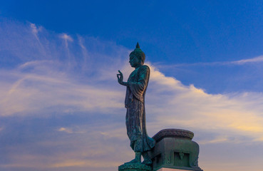 Fototapeta premium Standing buddha for worship in Phutthamonthon Park with sunset sky and reflective light,beautiful background