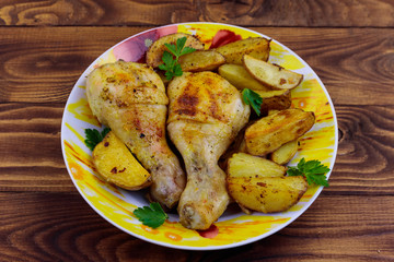 Baked chicken drumsticks with potatoes in a plate on wooden table