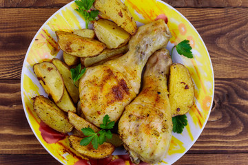Baked chicken drumsticks with potatoes in a plate on wooden table