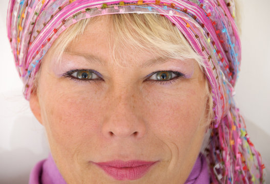 Beaming natural woman face (not retouched) wearing bohemian style head scarf. Dressed according actual fashionable color trends, person is looking straight into camera.