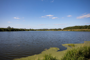 Beautiful summer landscape with river and greenery. Reflection of the sky in the water