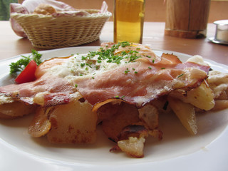 Typical South Tyrolean dish with speck, fried eggs, potatoes and chive